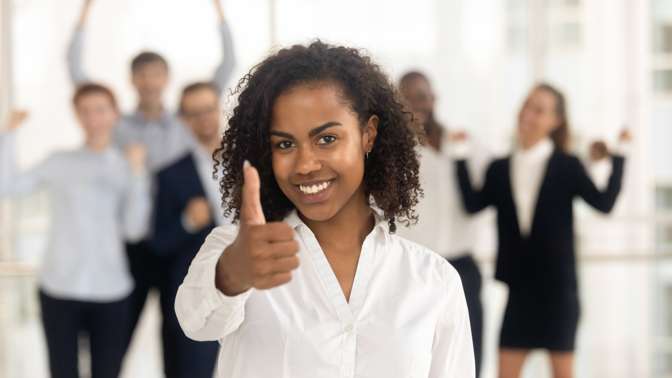 No 'single fix' for SA's talent retention issue Smiling African female employee giving thumbs up with supportive team in background, symbolizing successful staff retention and positive workplace culture